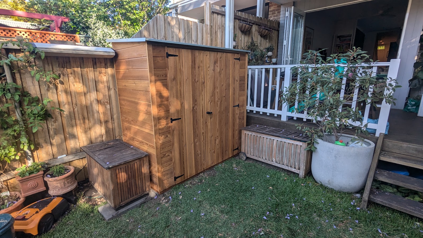 Timber garden shed with double doors and a matching storage box beside a deck