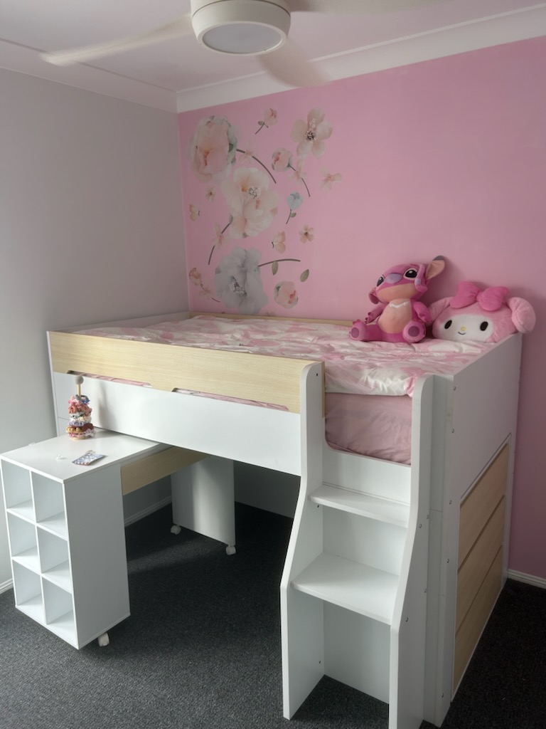 White kids' loft bed with built-in desk, shelves and stairs, assembled in a pink bedroom